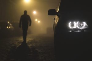 Bilens strålkastare på en dimmig bakgrund med en vandrande man. Kväll-natt